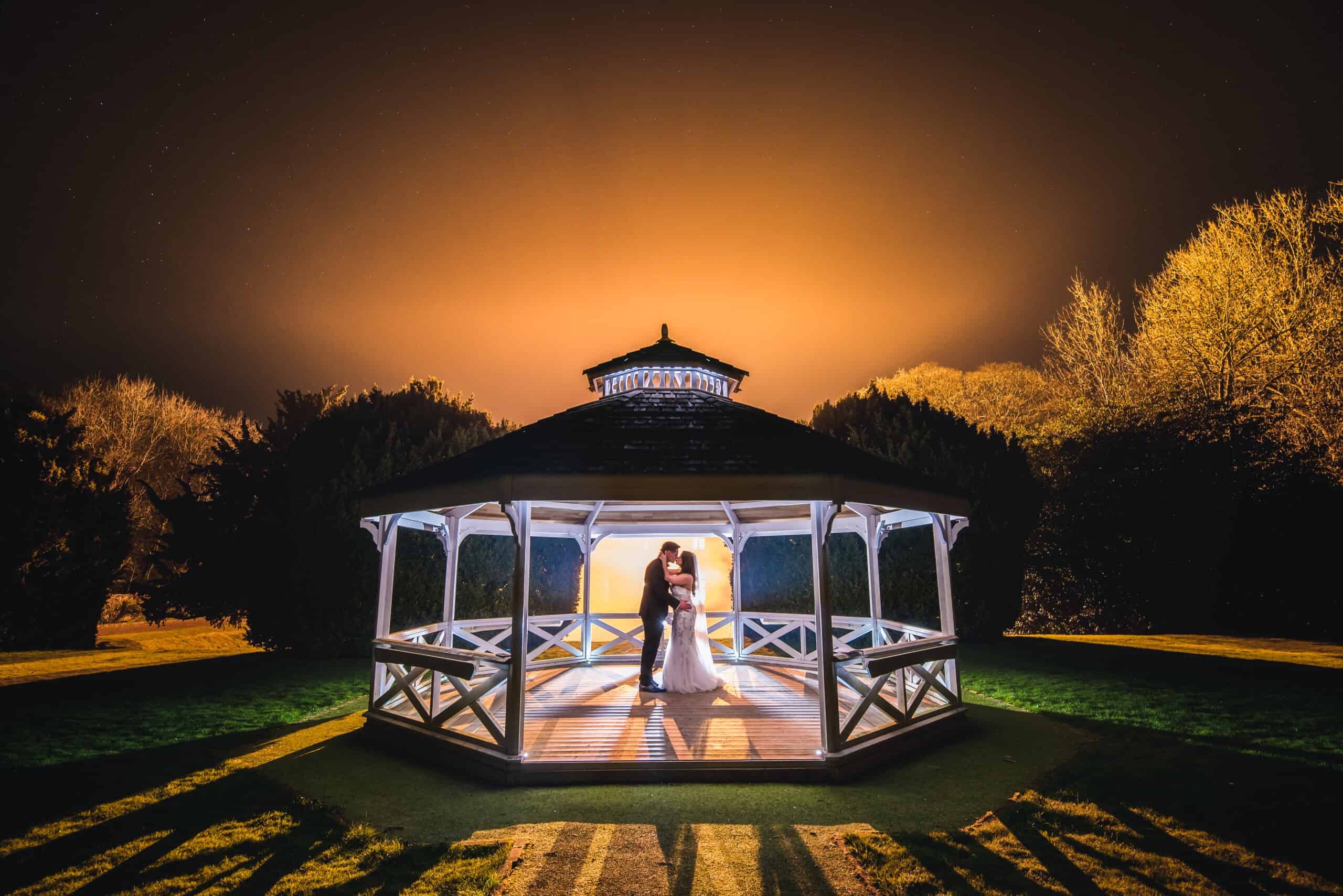 A couple in the illuminated garden Bandstand at night
