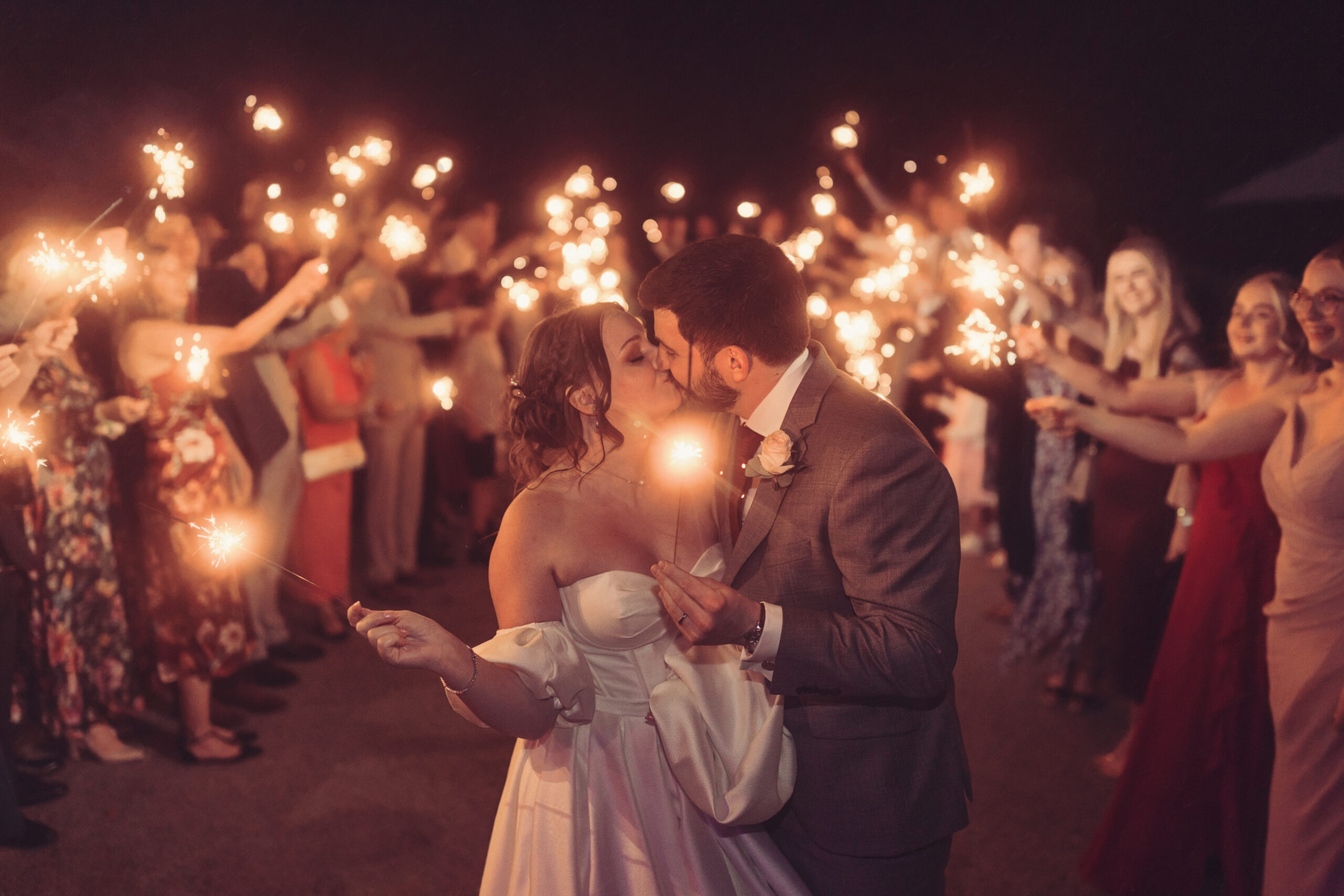 A sparkler tunnel, the couple kissing as guests hold sparklers overhead