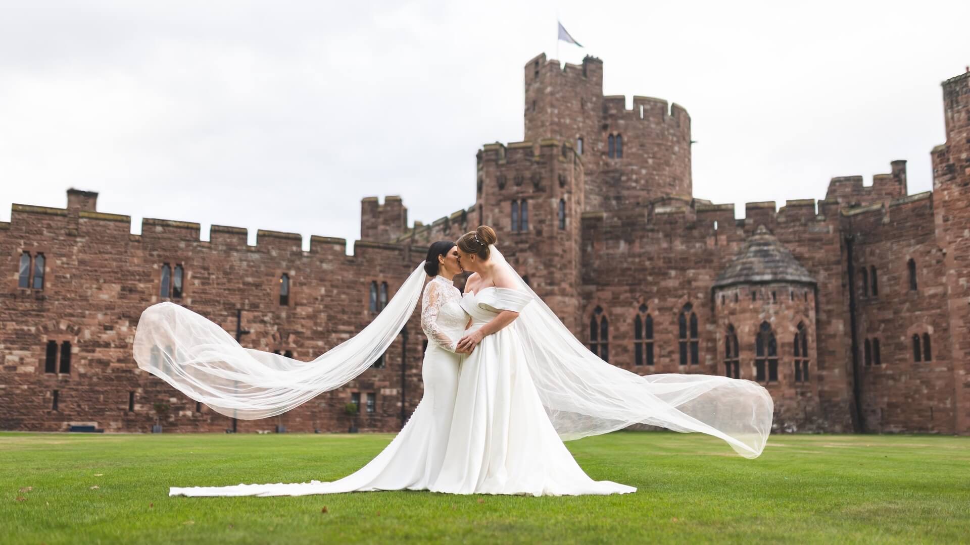 Two brides on the lawn, veils sweeping, the castle behind