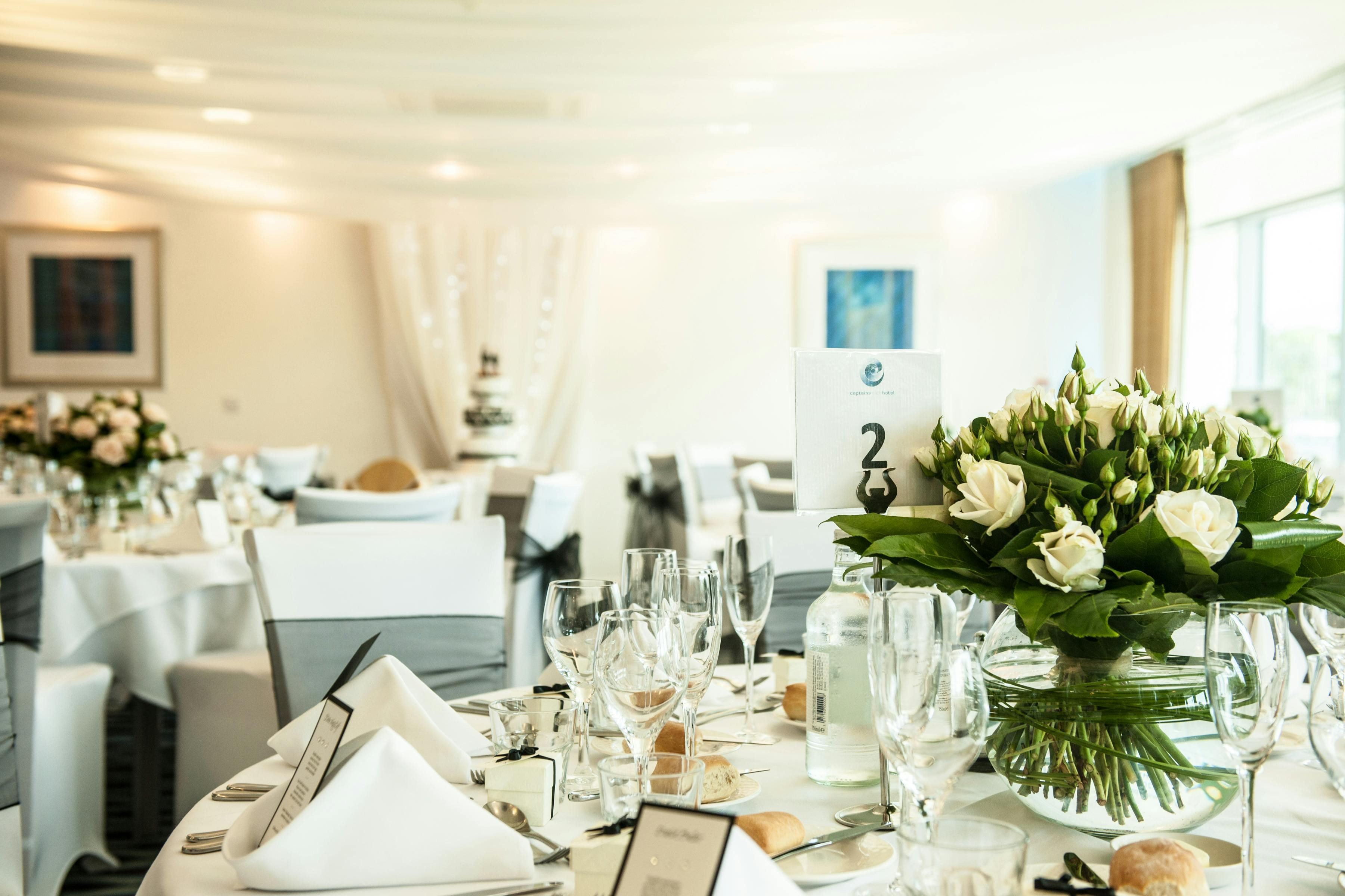 A round wedding table dressed with white roses and folded linen beneath drapes