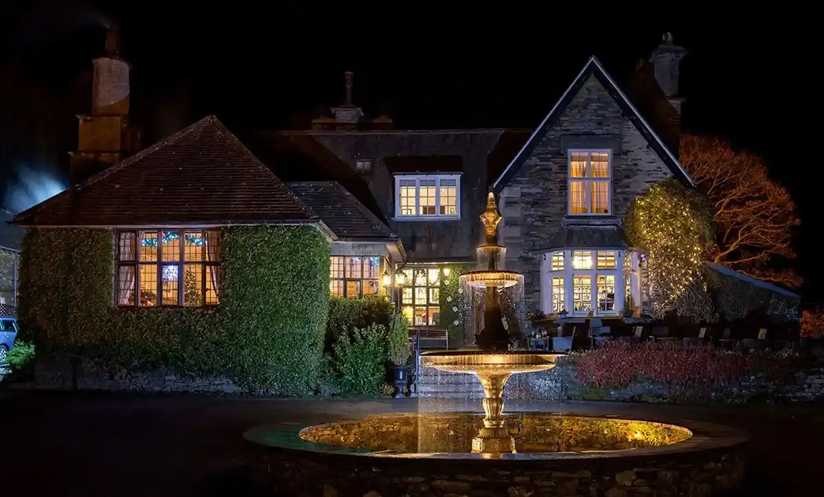 The house at night, the windows lit and the fountain floodlit