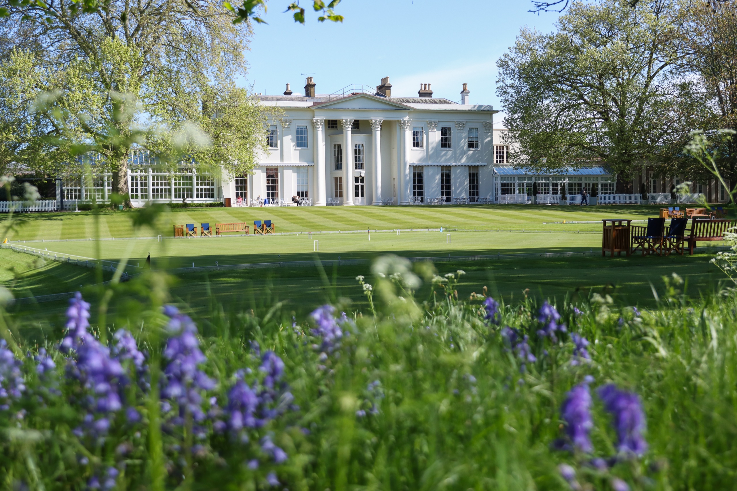 The clubhouse beyond the croquet lawn, with spring bluebells