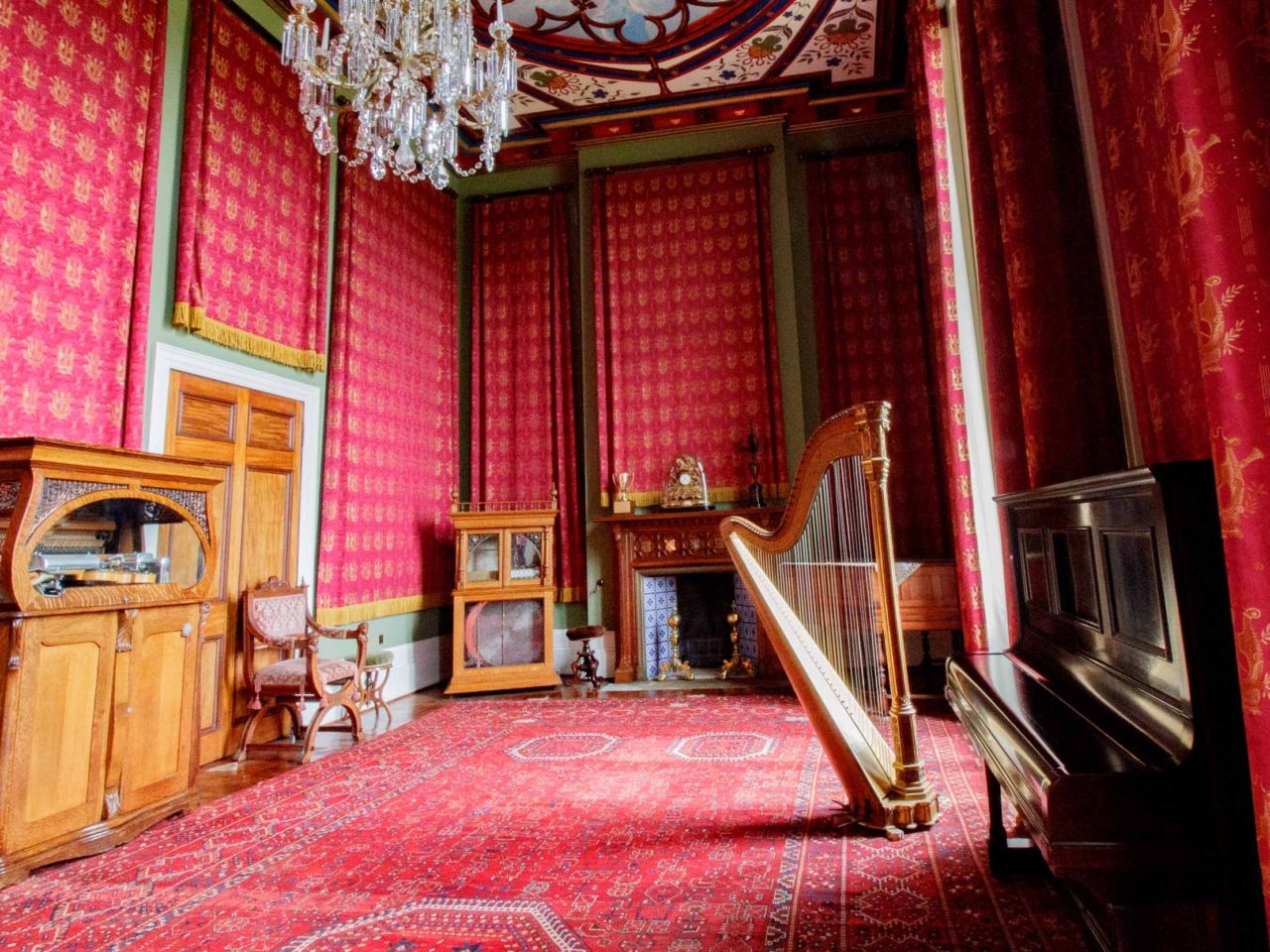 A crimson bedroom with a harp, four-poster and chandelier