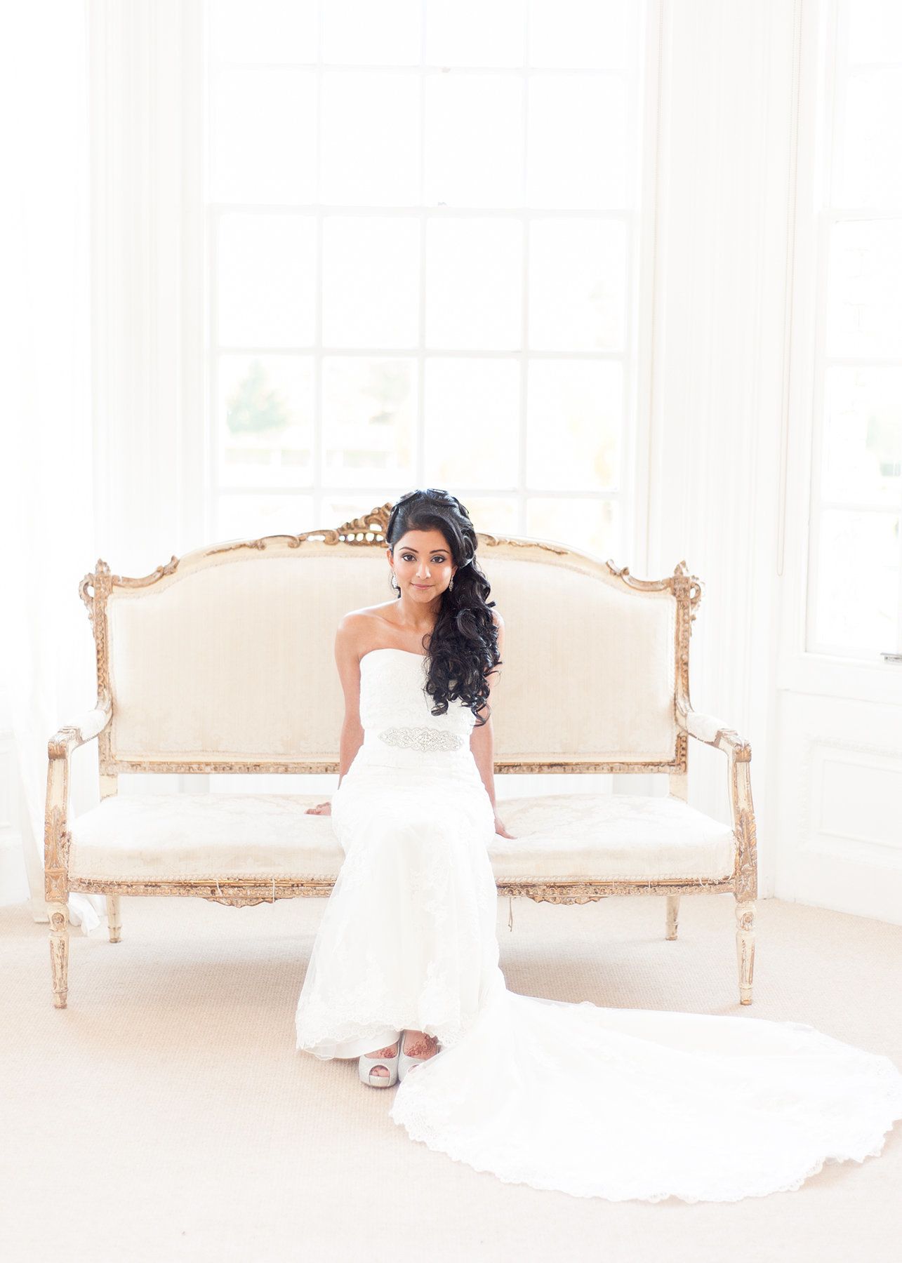 A bride seated on a gilt vintage sofa, fitted lace gown