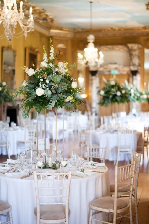 Round reception tables in white linen with tall floral centrepieces beneath a chandelier