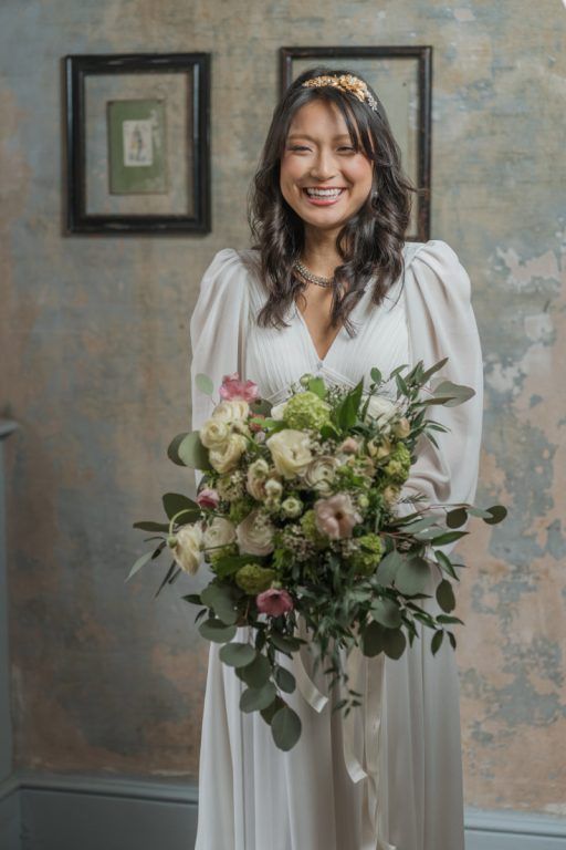 A bride laughs, holding a bouquet of rose, hellebore and eucalyptus