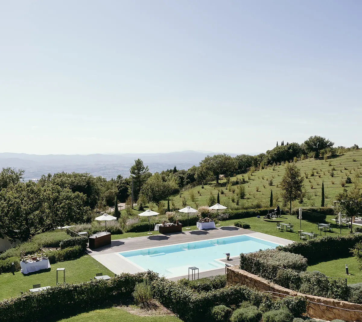 A pool and its parasols on a terraced hillside in Umbria, the plain beyond