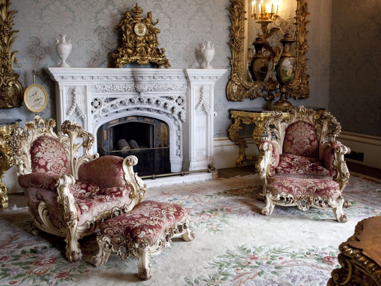 An ornate white marble fireplace framed by gilded armchairs