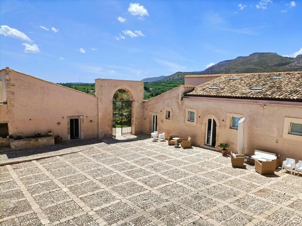 The courtyard framed by arched stone facades, the Iblei Mountains beyond