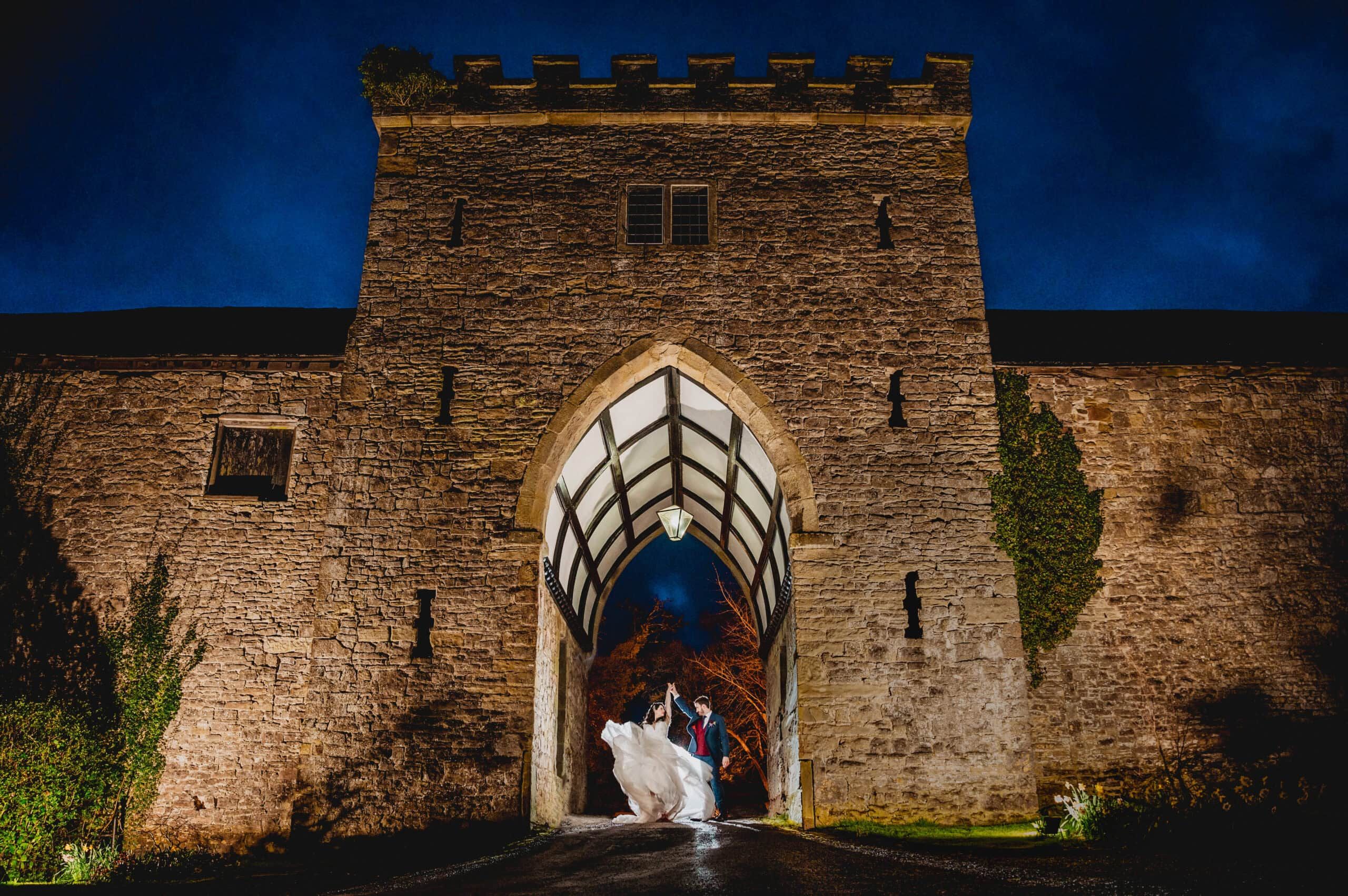 A couple beneath the floodlit gatehouse tower and pointed arch after dark
