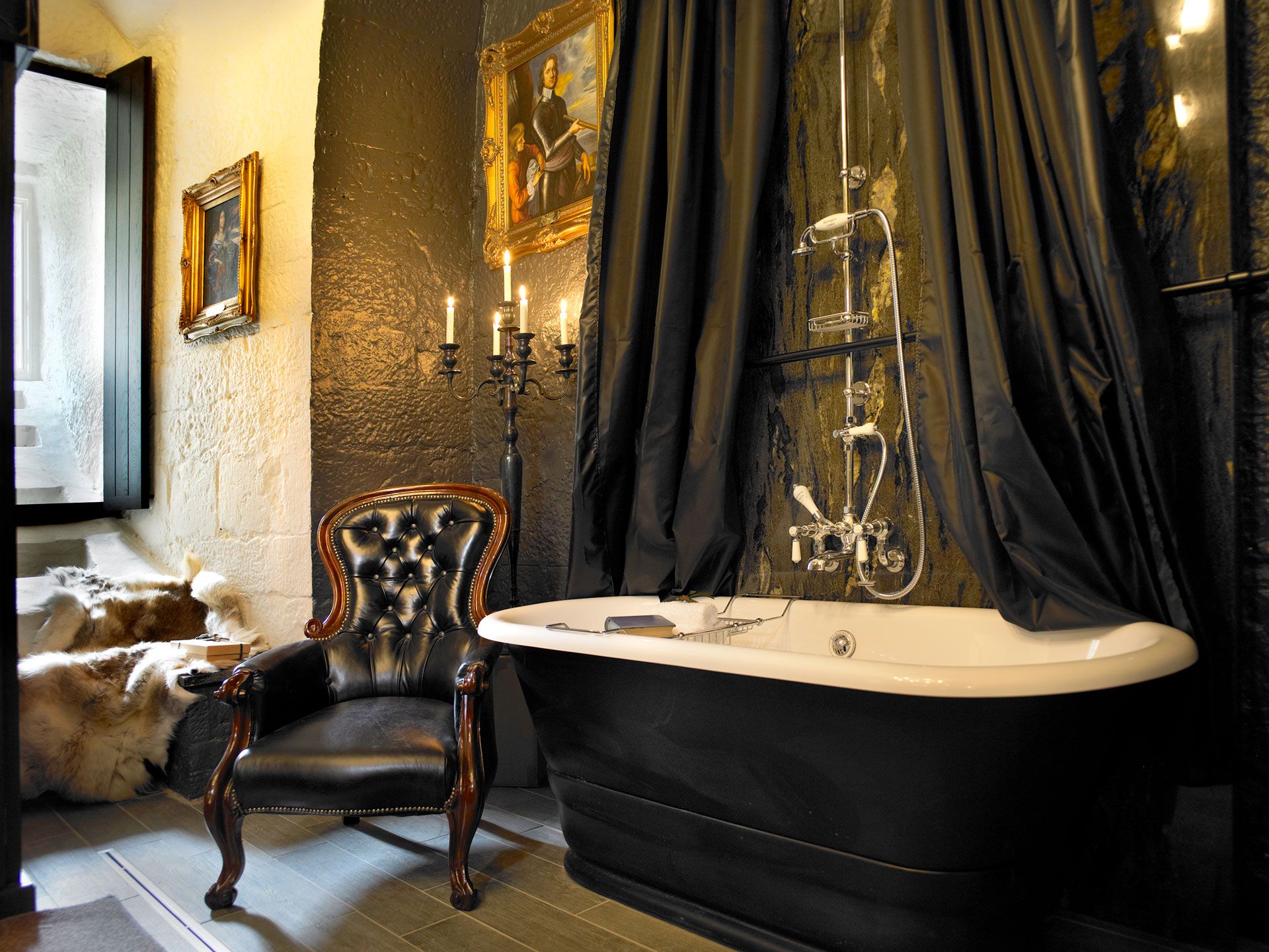 A black roll-top bath beneath gilt portraits