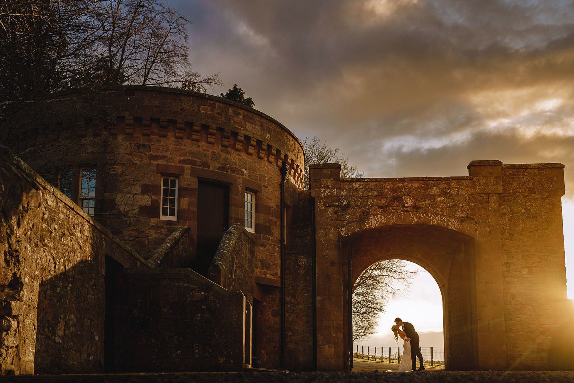The twin-tower keep floodlit at dusk, a couple in the gatehouse arch, Borthwick Castle, North Middleton, Scotland