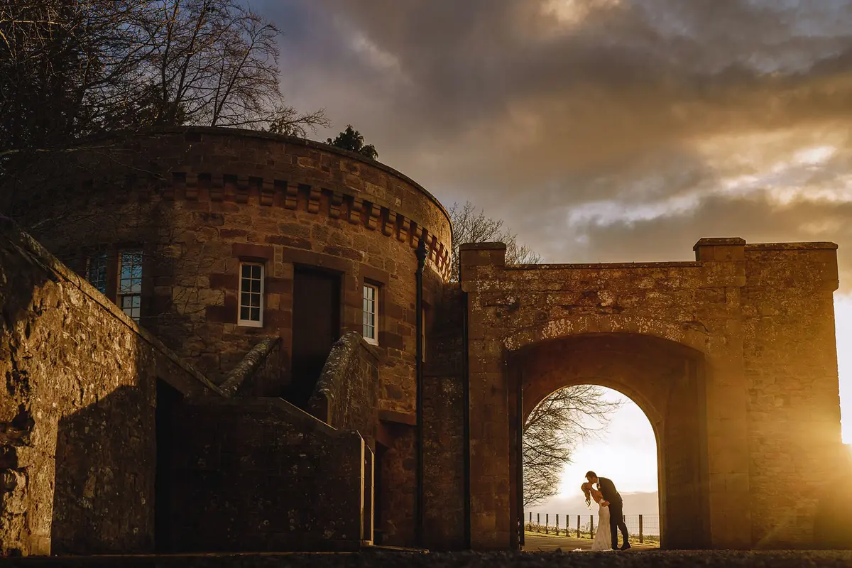The twin-tower keep floodlit at dusk, a couple in the gatehouse arch, Borthwick Castle, North Middleton, Scotland