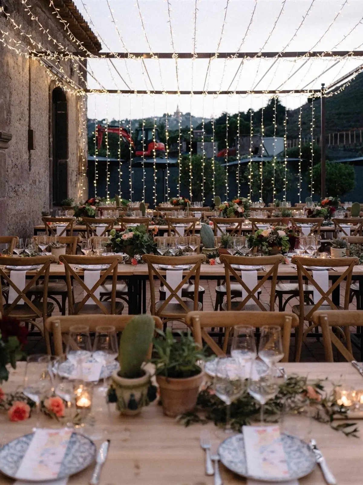 Long reception tables laid beneath a canopy of fairy lights at dusk