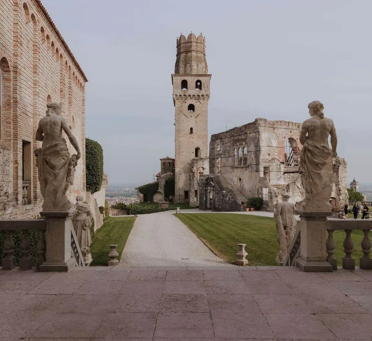 A ruined medieval tower and cloister on a Veneto hilltop, guarded by weathered stone lion statues