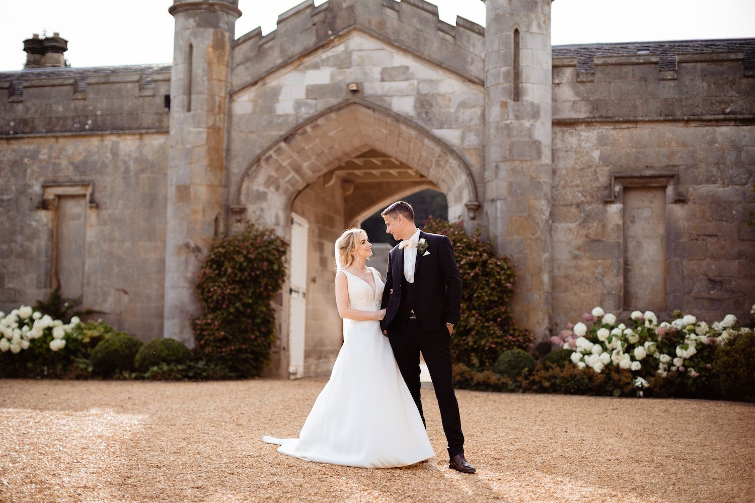 A bride and groom beneath a castle archway dressed with white flowers