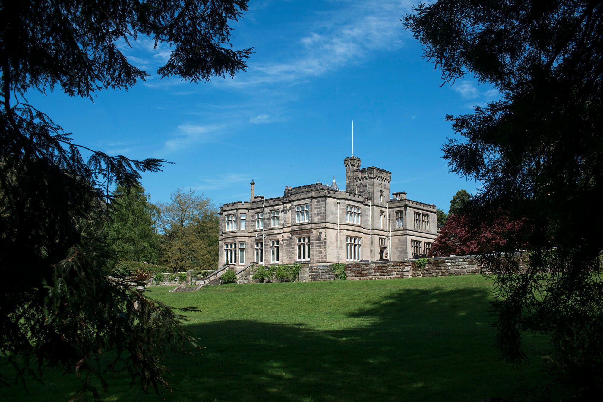 The manor house beneath a wide sky, its gables and turrets above sweeping estate lawns, Hampton Manor, Hampton-in-Arden, England