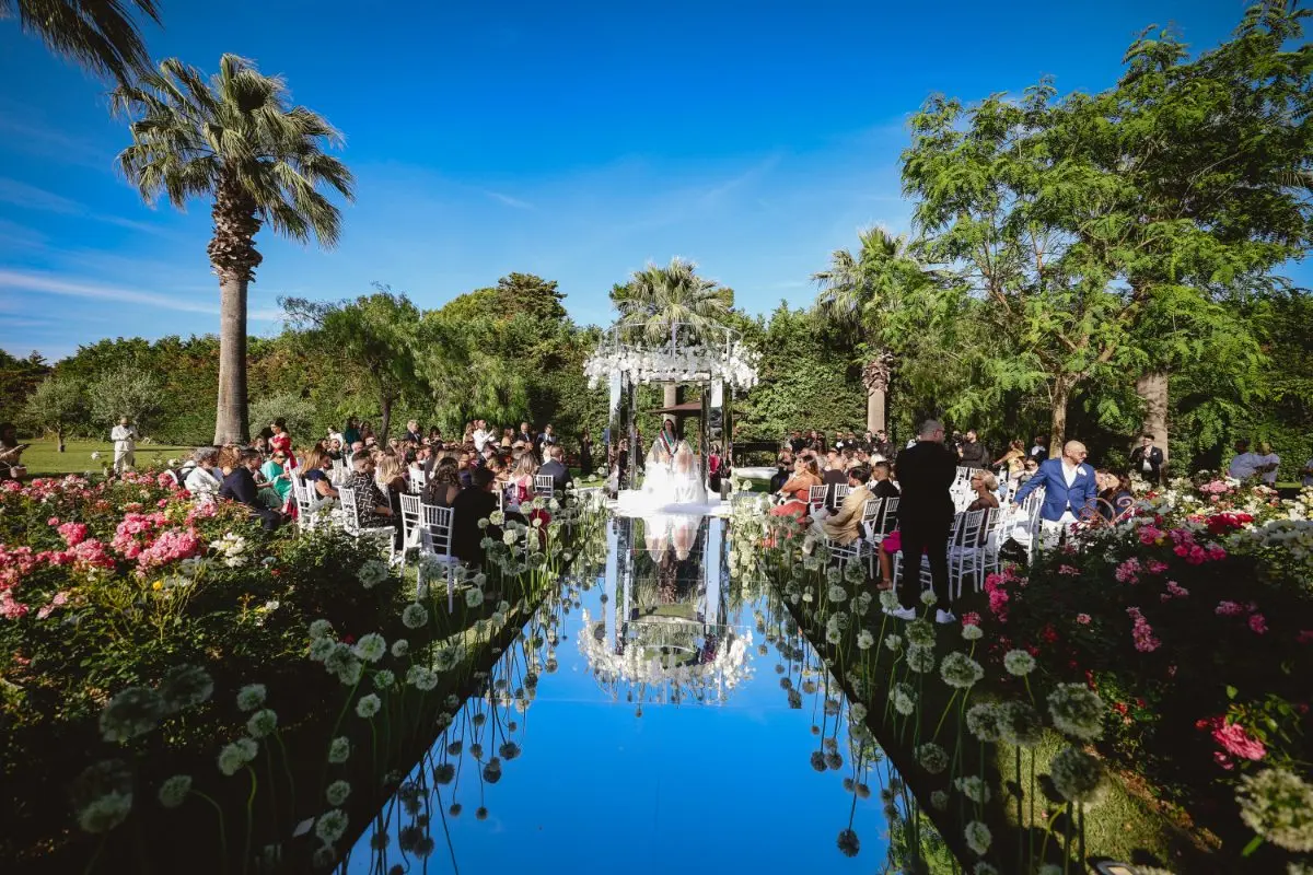 A ceremony aisle laid across mirrored water, under palms