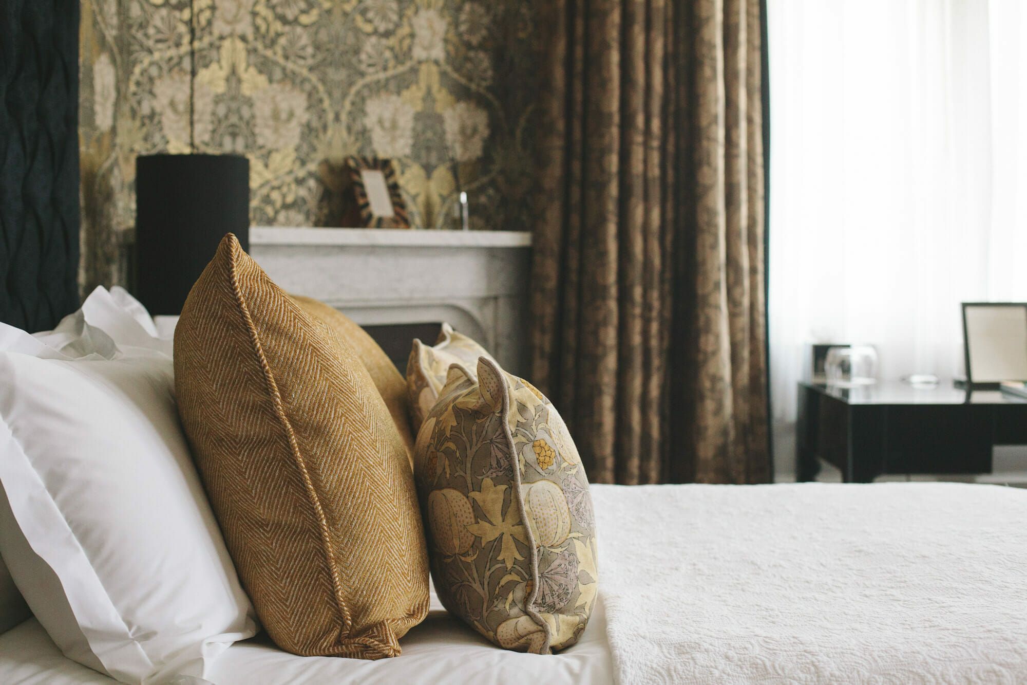 A bedroom with a marble fireplace, gold cushions and patterned drapes