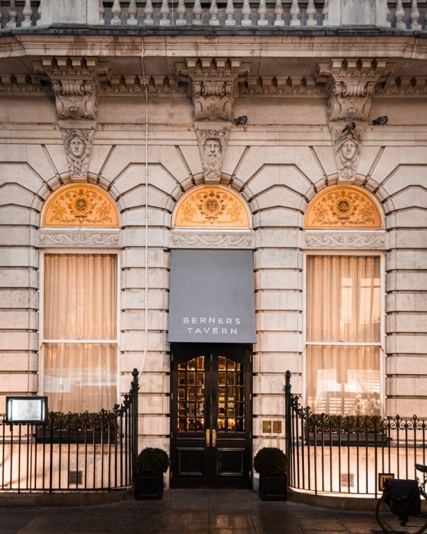 The lit facade and arched windows of Berners Tavern on Berners Street at dusk