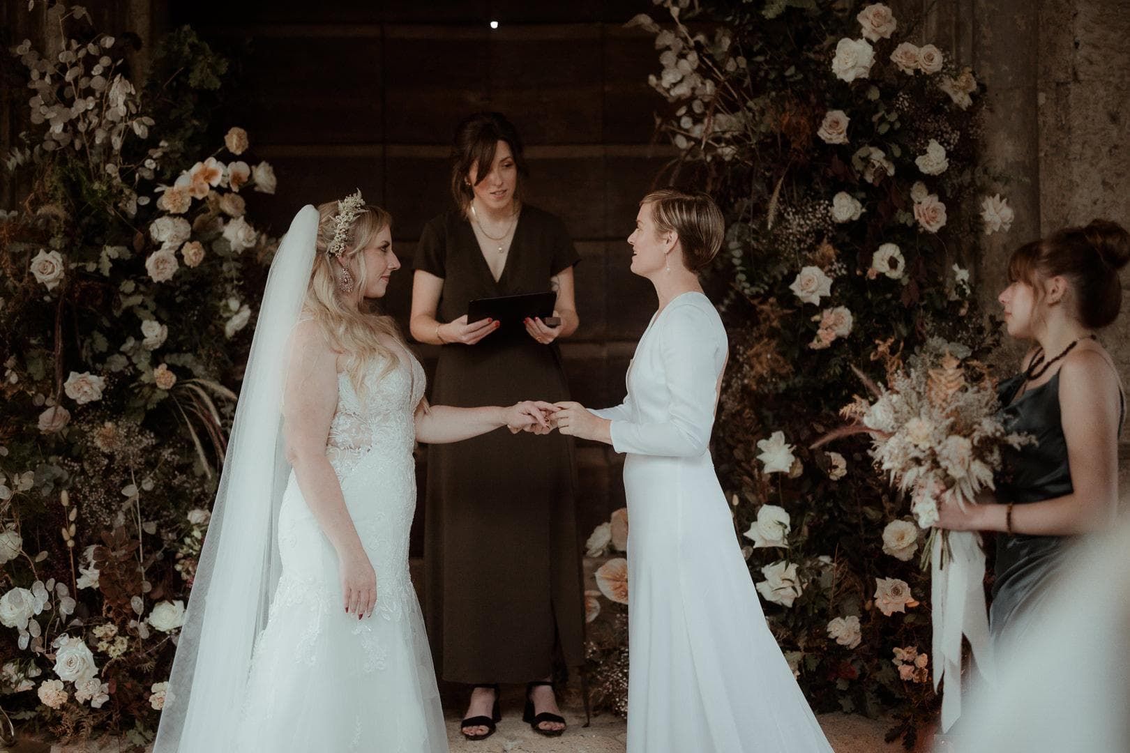 Two brides taking their vows in front of a wall of flowers
