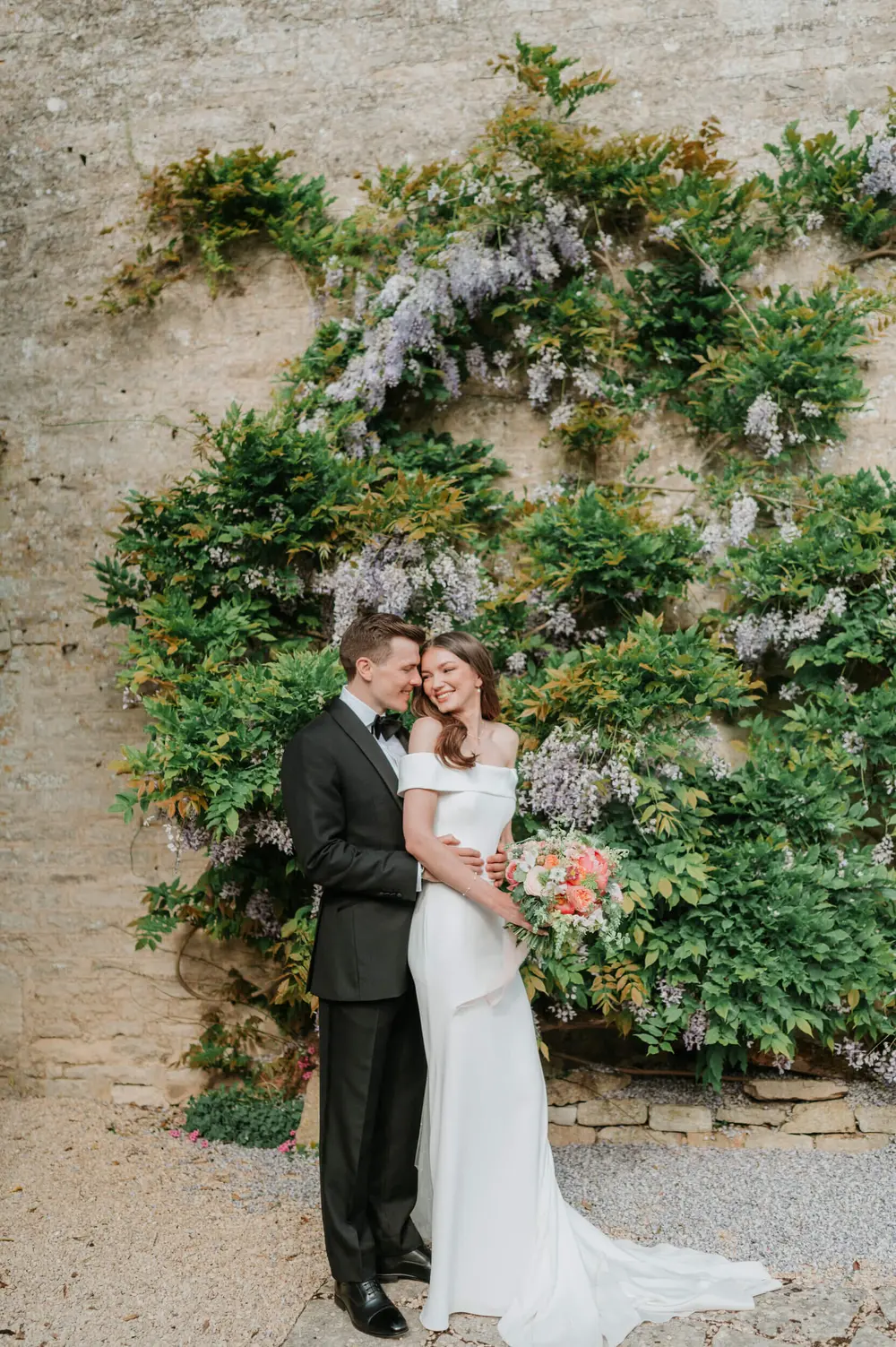 The couple against a wisteria-covered wall at Caswell House