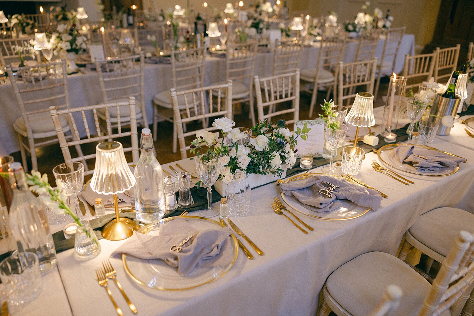 A close table setting, gold-rimmed glass and white blooms