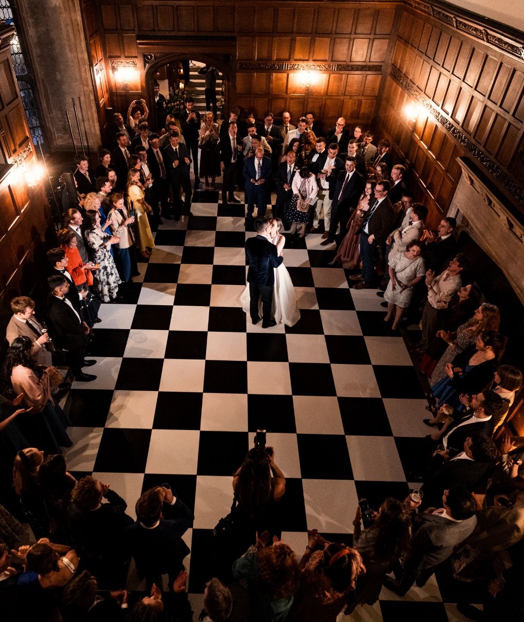 Guests dancing on a black-and-white chequered floor in the panelled hall at night