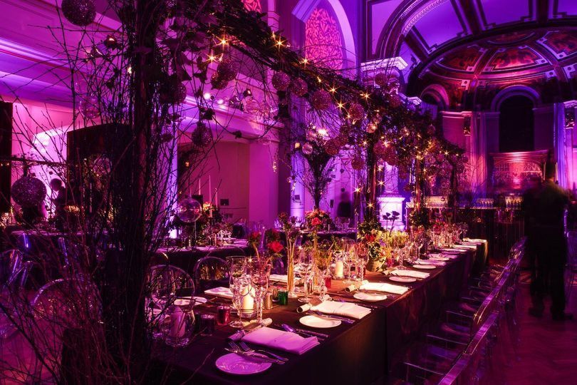 A dramatic purple-lit long banquet table dressed with hanging blossom branches under the galleries, One Marylebone, London, England