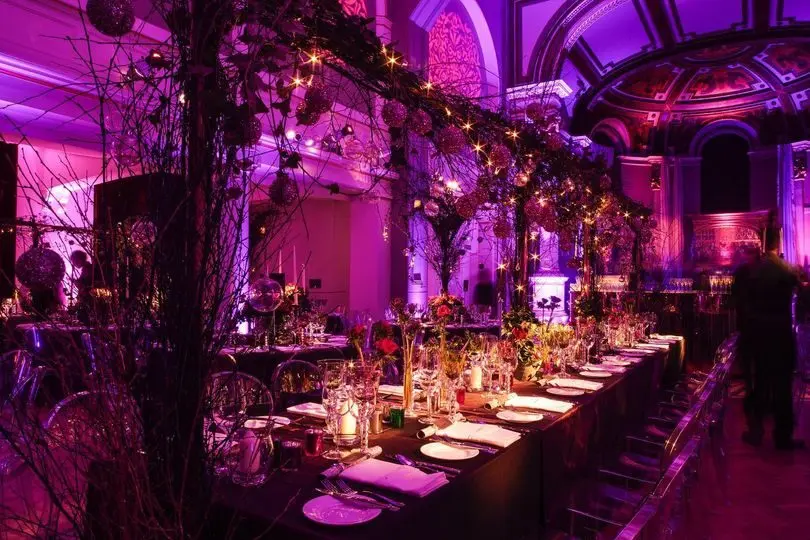 A dramatic purple-lit long banquet table dressed with hanging blossom branches under the galleries, One Marylebone, London, England