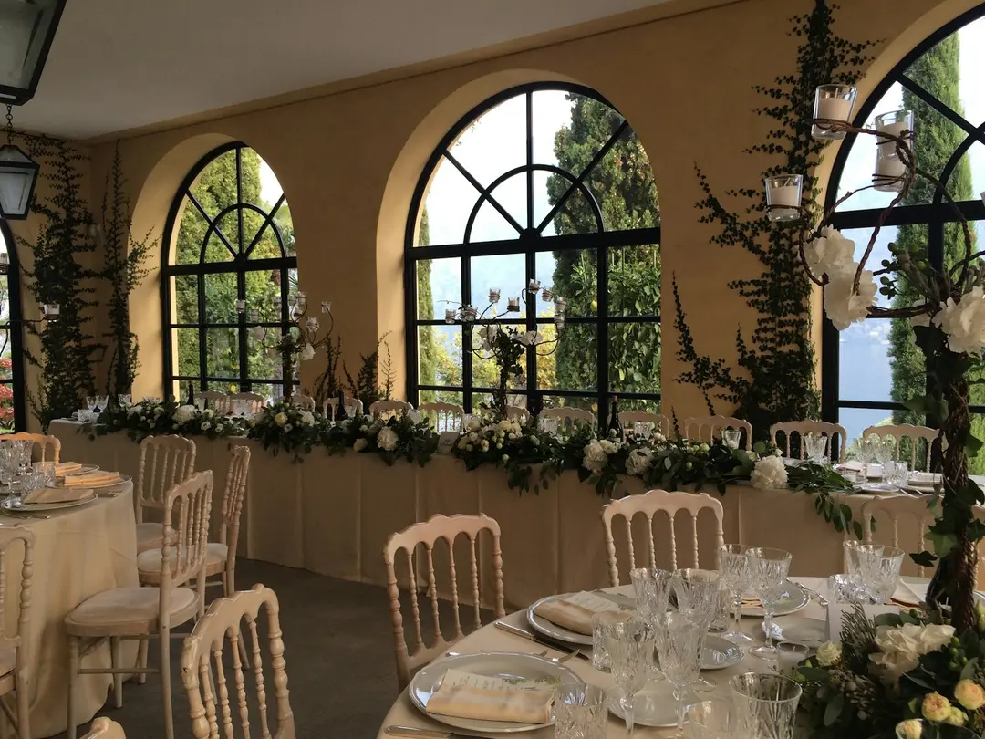 The Loggia Segre set for a wedding dinner, arched windows onto the cypresses and lake, Villa del Balbianello