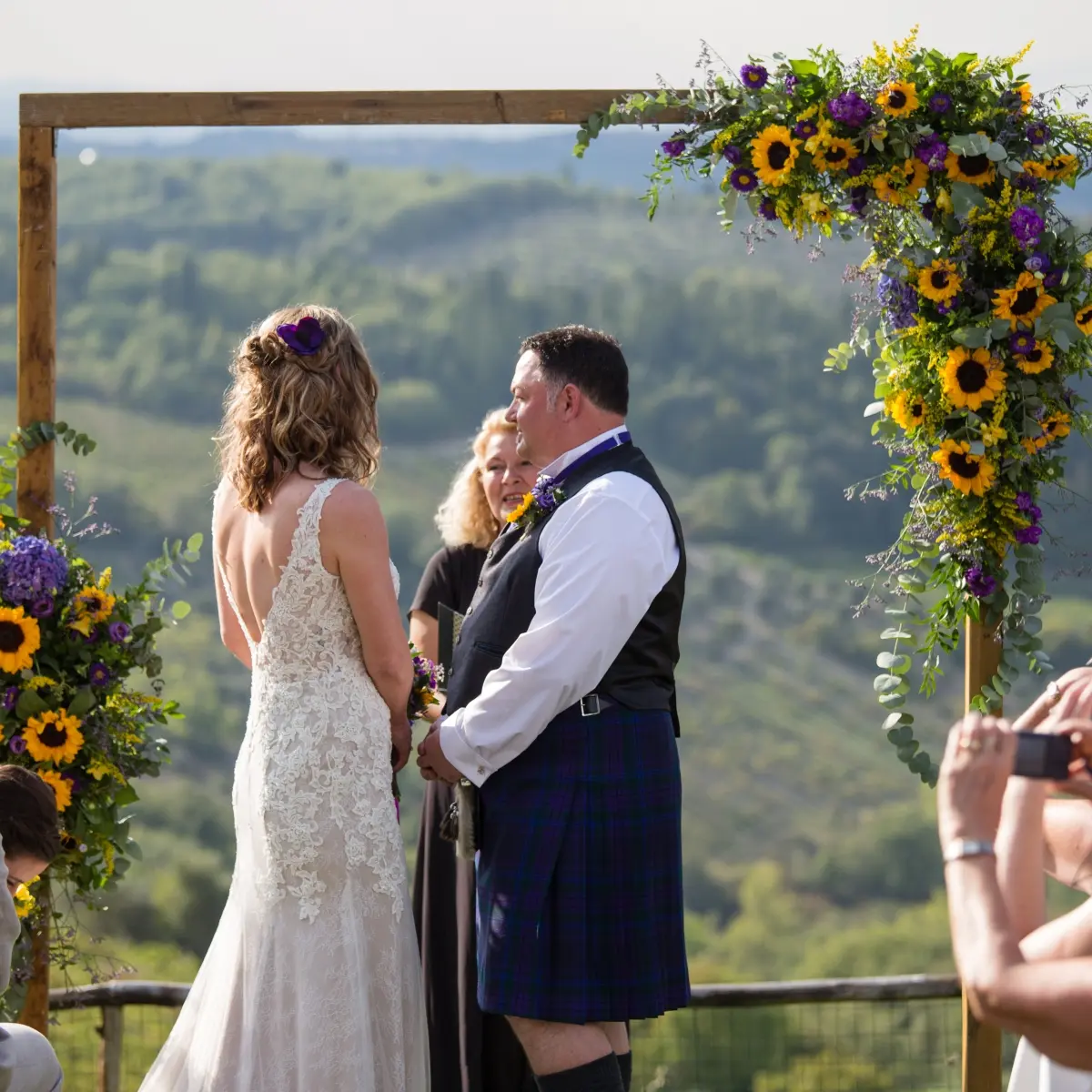 A couple at a sunflower arch, the groom in a Scottish kilt, overlooking Tuscan hills