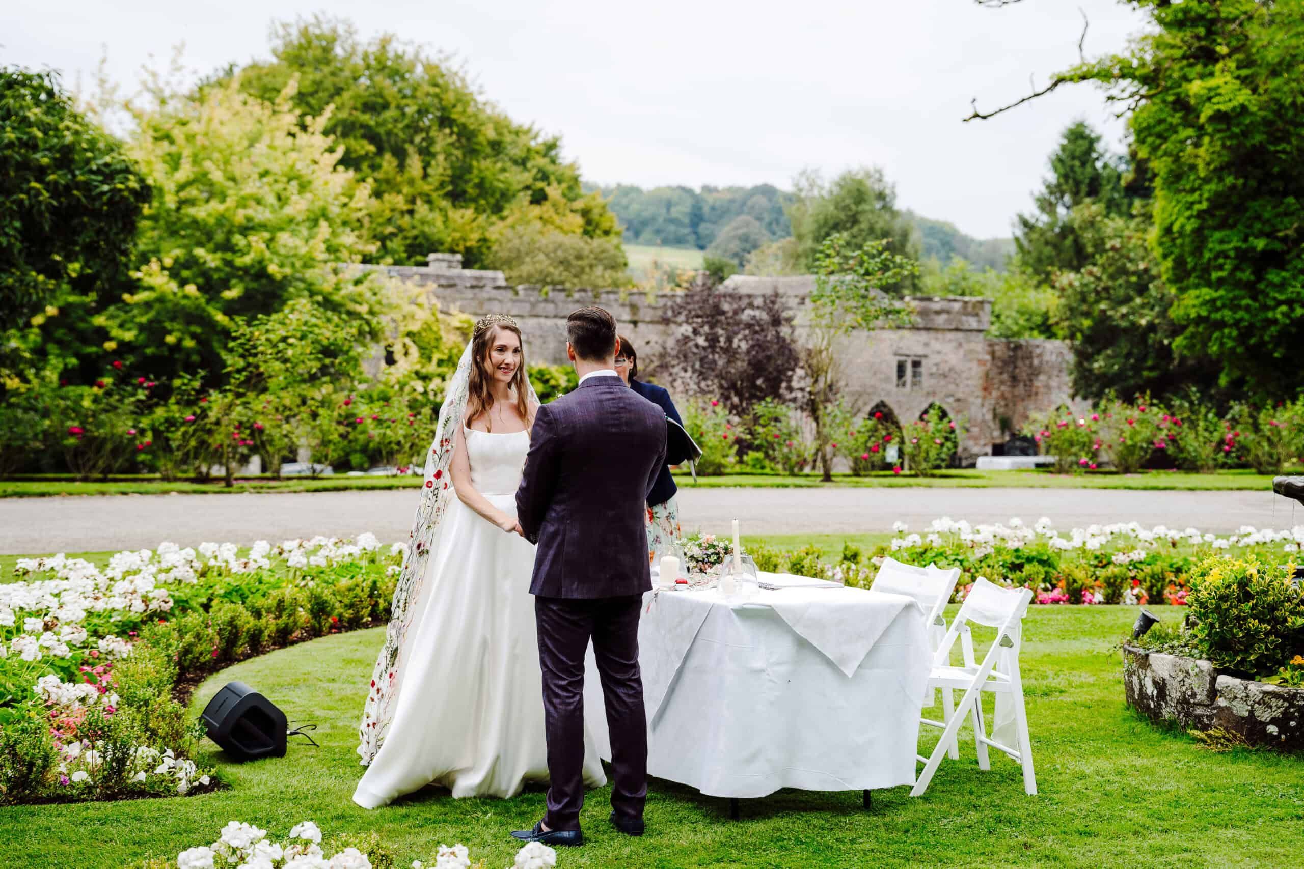 A ceremony by the garden Bandstand, the couple at the table amid flower beds and the castle wall beyond