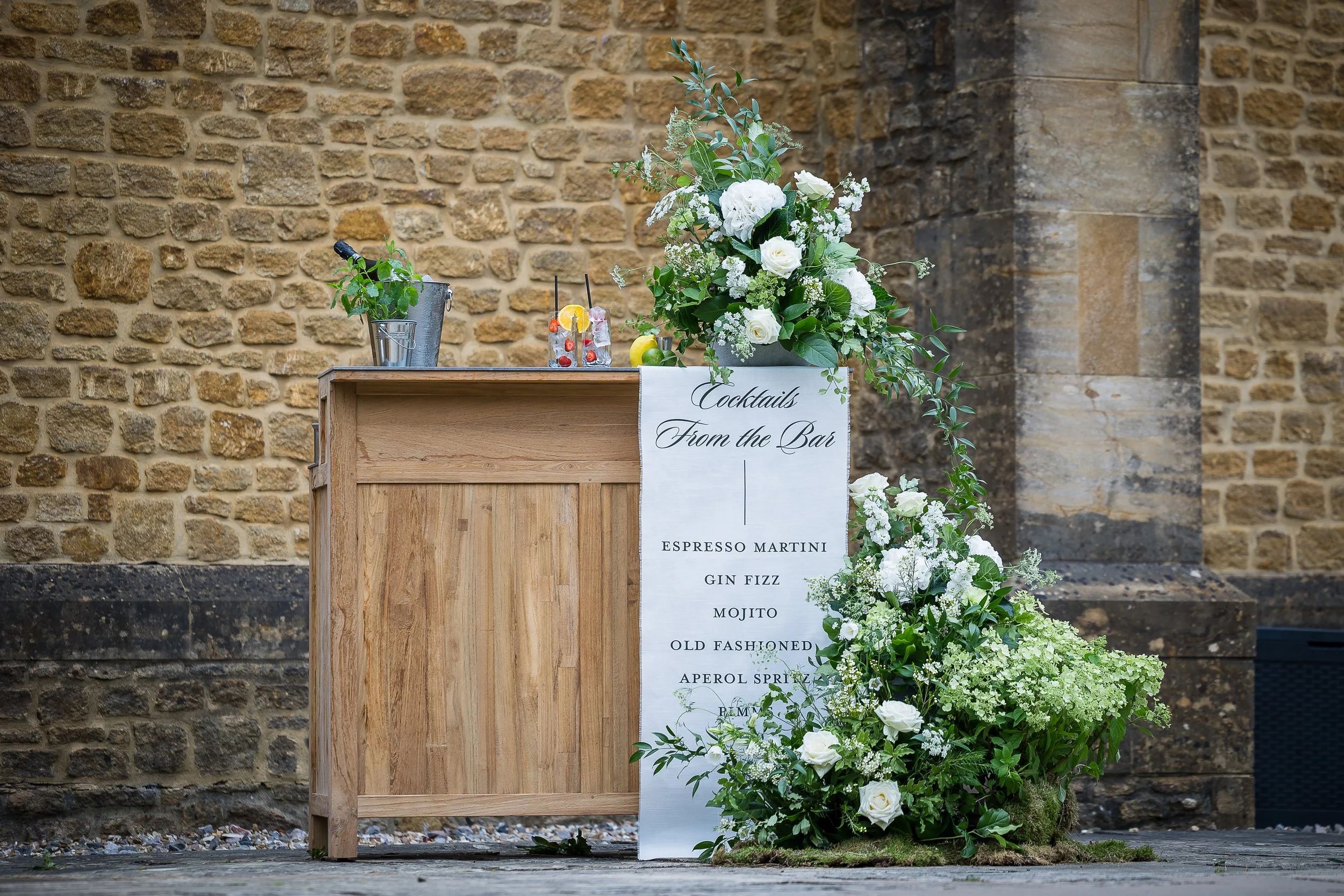 A cocktail bar, dressed with garden flowers against hamstone