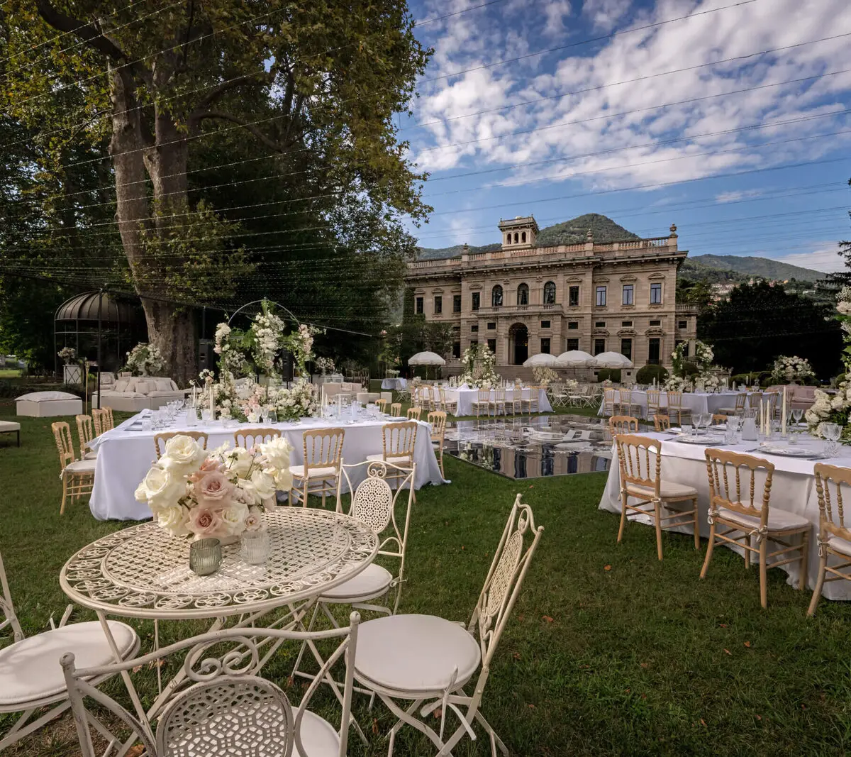 A garden reception laid across a villa's lawn, long tables reflected in a mirrored dance floor