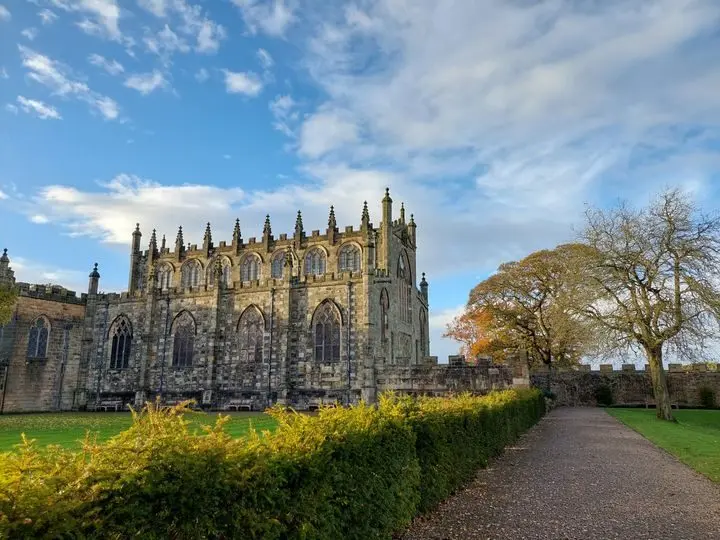 The Gothic east wing and St Peter's Chapel, a garden path and clipped hedge under blue sky, Auckland Castle, Bishop Auckland, England