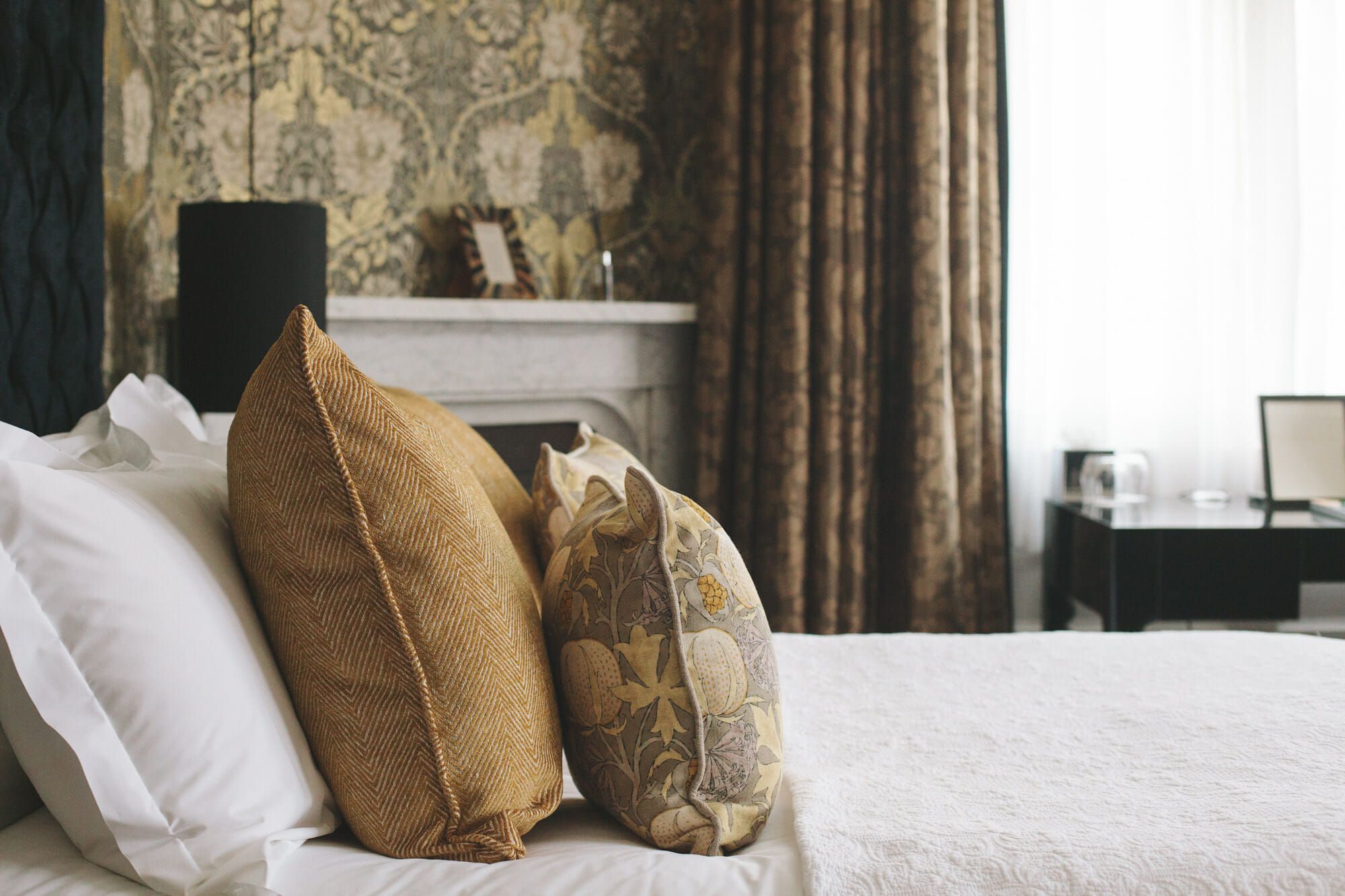 A bedroom detail, gold cushions on a white bed beside a fireplace