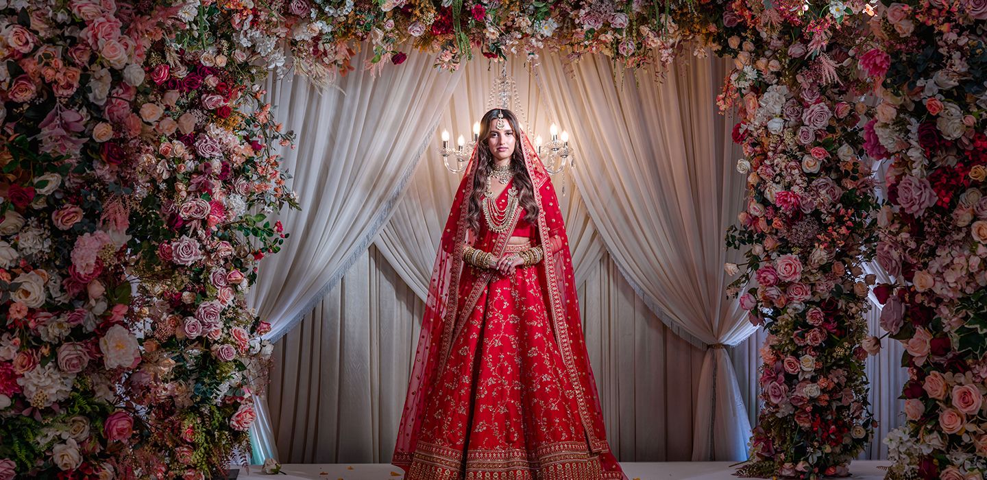A bride in a red lehenga, beneath a floral arch