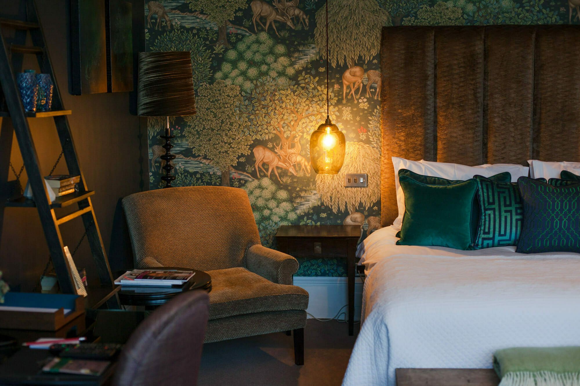 A softly lit bedroom with a velvet armchair and richly patterned walls