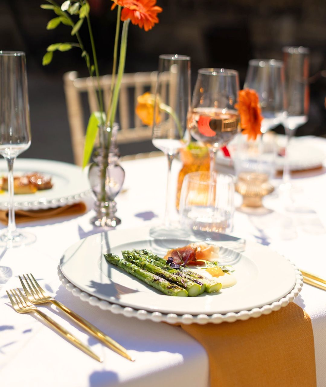 A plated first course of asparagus, with orange blooms and gold cutlery on the table
