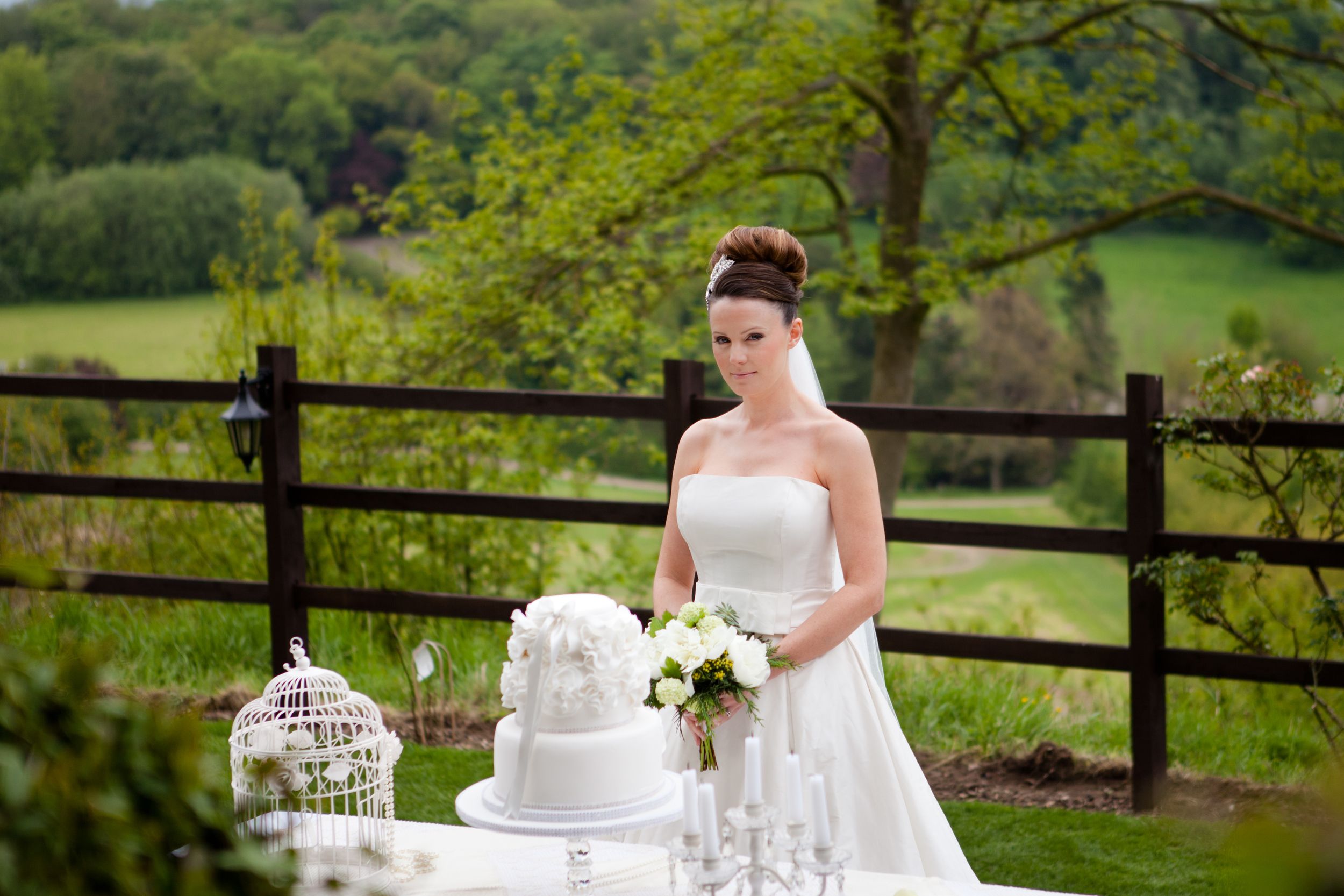 A bride beside a styled reception table, birdcage and wedding cake behind her