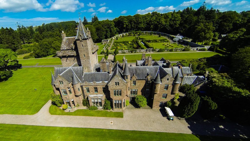 An aerial view of the turreted baronial castle in its wooded grounds and gardens, Guthrie Castle, Forfar, Scotland