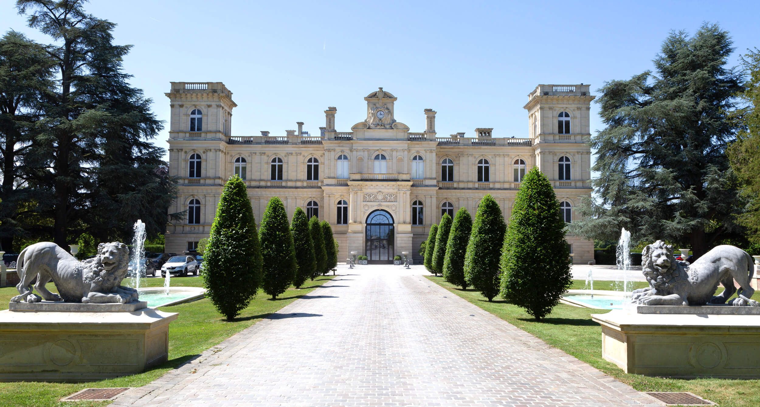 The front façade of a grand château with an avenue of lion statues