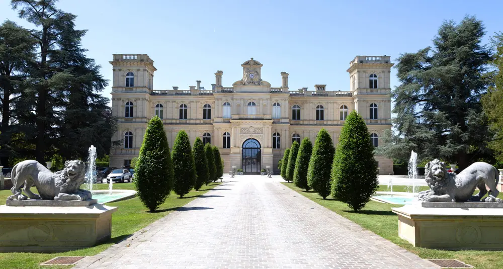 The front façade of a grand château with an avenue of lion statues