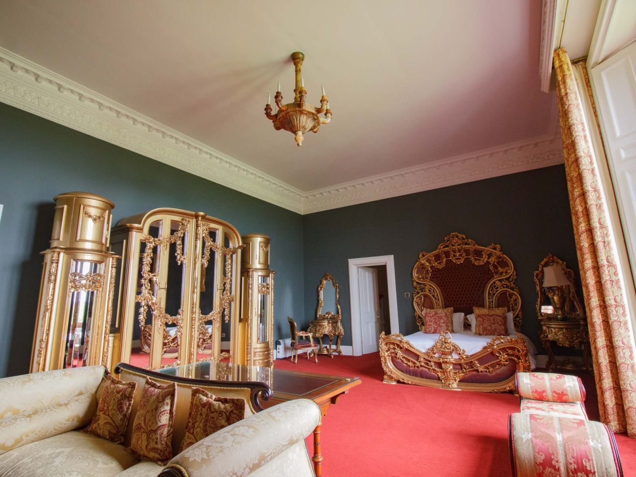 A sage-green bedroom with an ornately carved bed and a chandelier