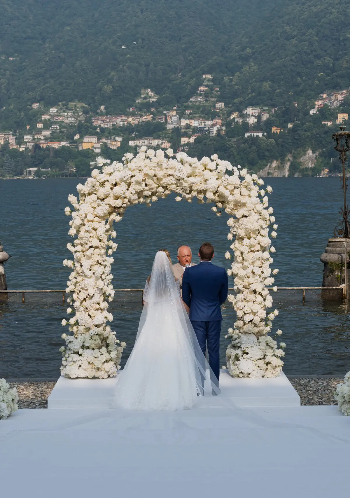 A ceremony at the water's edge on Lake Como, a white rose arch standing on the quay