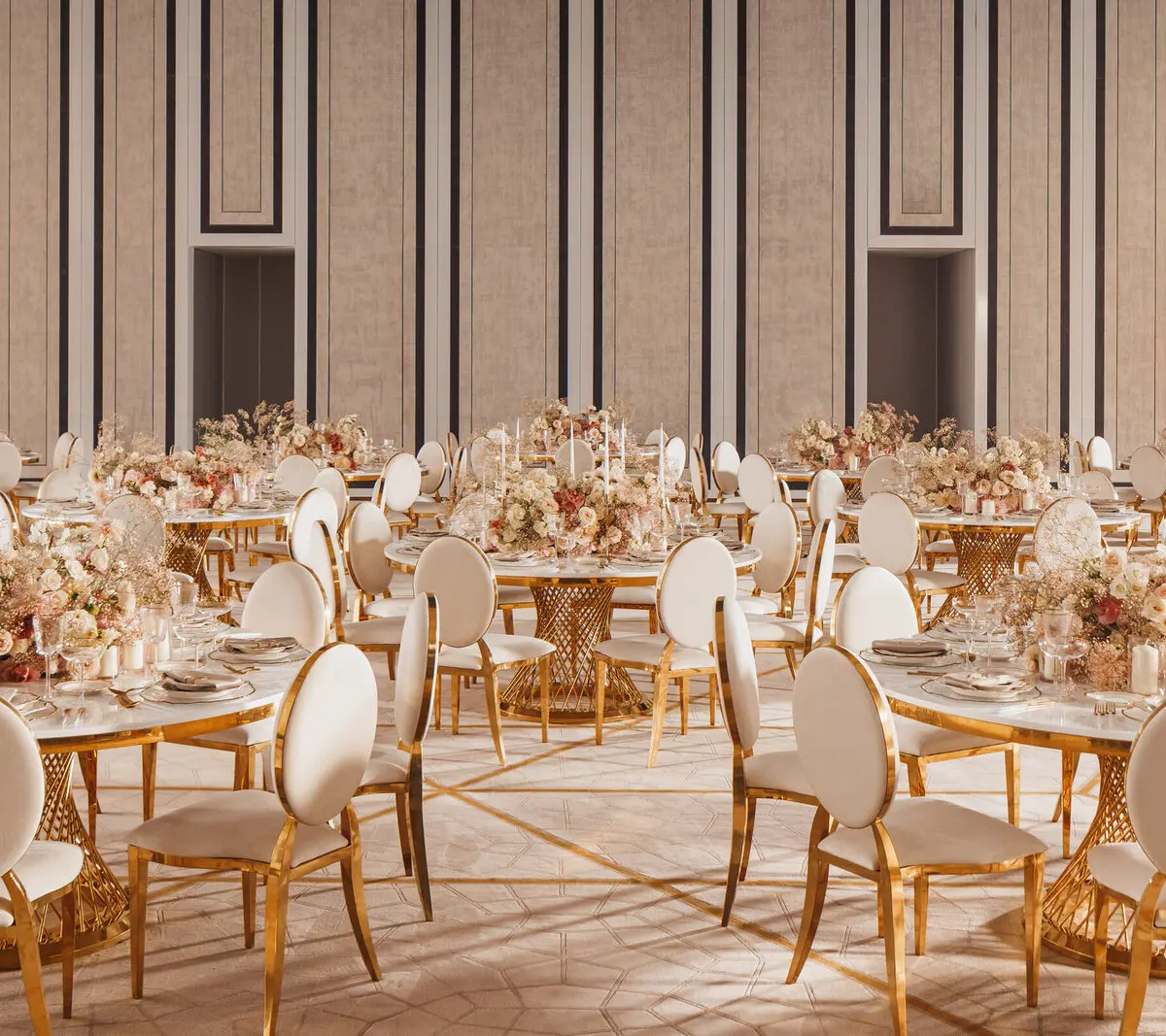 A gold-toned ballroom set for a wedding, dozens of round tables beneath striped panelled walls