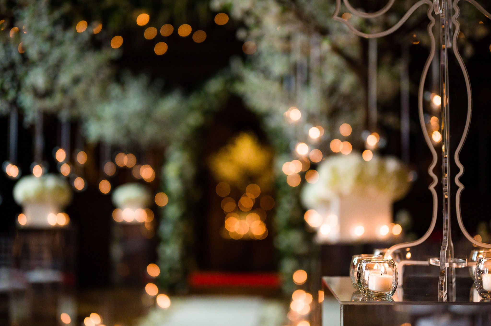 A candlelit evening reception detail, a foliage arch and glowing lights beyond