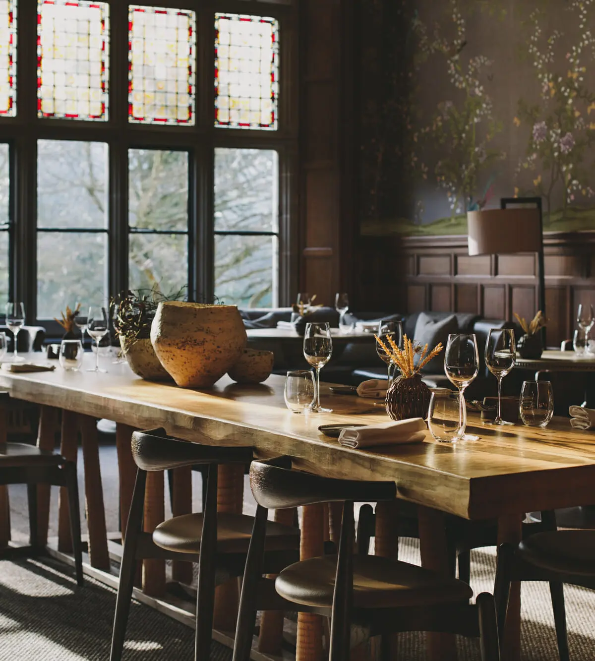 A panelled dining room set at a long table beneath stained glass