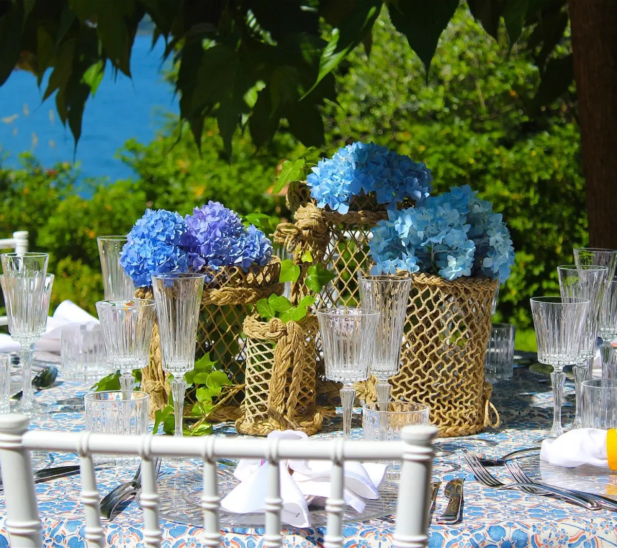 Blue hydrangeas in gold cachepots on a table set above the water